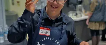 Happy Brew employee with branded apron holding up a cup