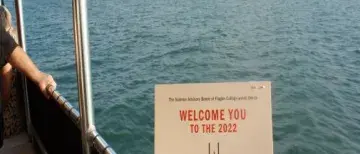 Someone is holding the Sunset Cruise invitation with water and a lighthouse in the background
