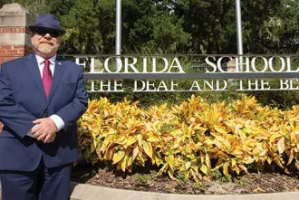 Flagler College Alum, Owen McCaul, stands next to the sign for the Florida School for the Deaf and the Blind