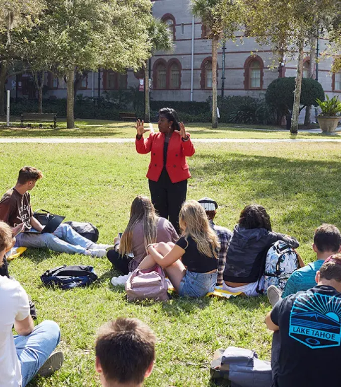 A professor teaching to their class of students who are sitting on the grass of the West Lawn